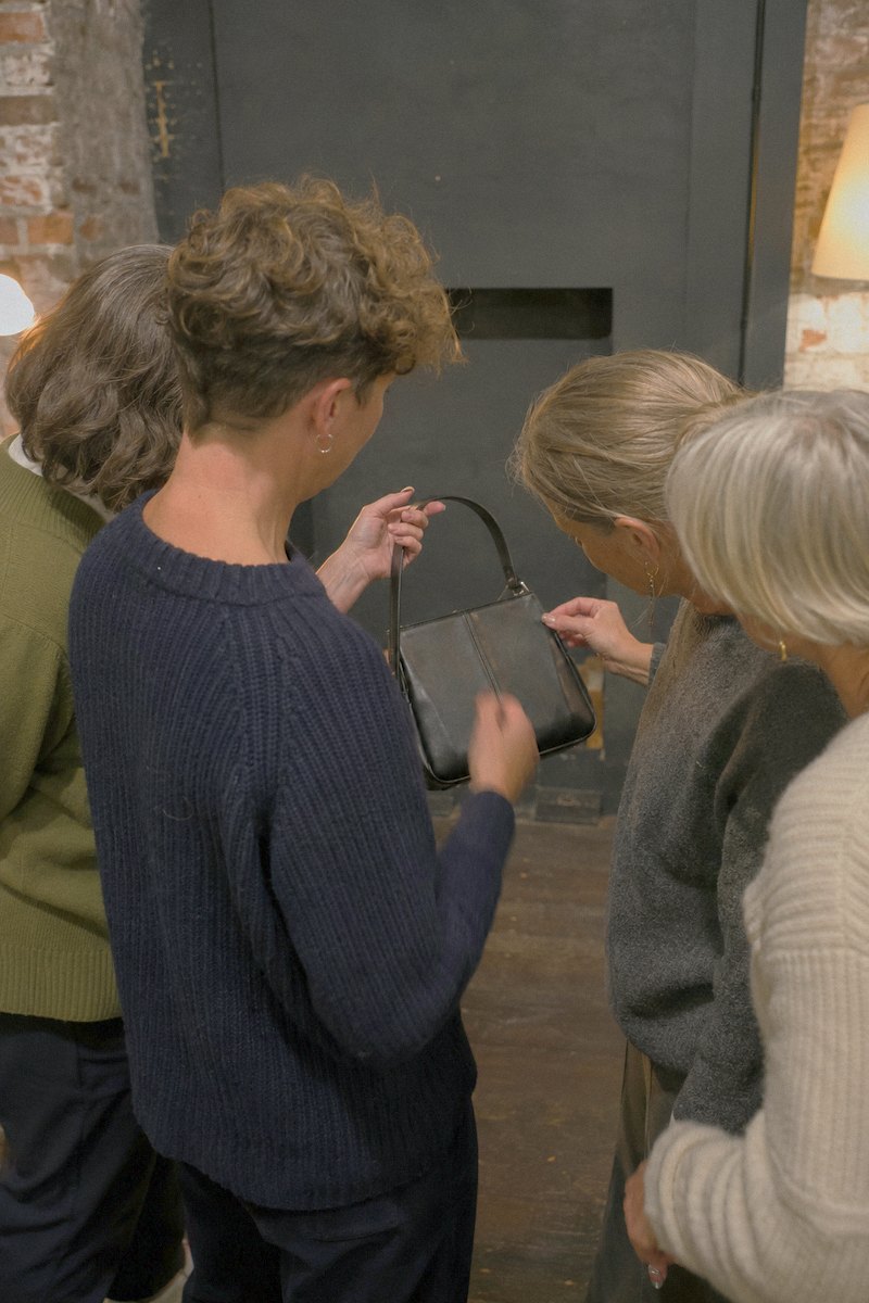 Four people standing close together, looking at a leather handbag one of them is holding